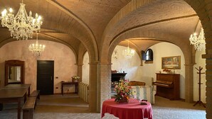Un vaste hall doté de voûtes en briques, de lustres, d’un piano et d’une table ornée de fleurs.