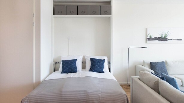 A modern bedroom with a bed, a built-in wardrobe, a sofa, and a wall-mounted artwork. - Modern Apartment Near the Beach (The Hague)