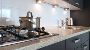 A modern kitchen with a gas stove, a pot on the burner, a sink, and dark cabinets. - Modern Apartment Near the Beach (The Hague)