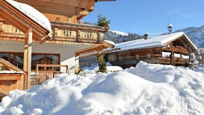 Un chalet en bois doté d’un balcon et d’un toit enneigé, entouré d’un paysage hivernal et de montagnes.