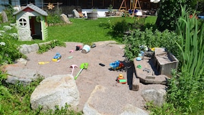 Un jardin avec un espace de jeux, comprenant un petit abri, des rochers et des jouets pour enfants.