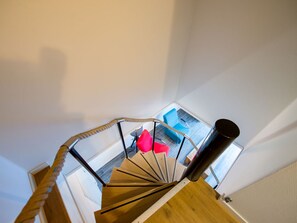 A spiral staircase with wooden steps and metal railings, leading to a room with a blue chair and a red pillow. - Holiday Home in Biggekerke Near the Beach (Biggekerke)