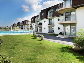 Una hilera de edificios modernos de varios pisos con balcones, piscina y césped bien cuidado.