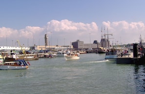 A marina with multiple boats docked, a large building in the background, and a clear sky.