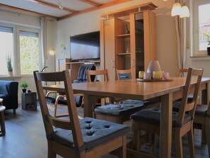 Un coin repas avec une table et des chaises en bois, un téléviseur placé au-dessus de la table et une bibliothèque en arrière-plan.