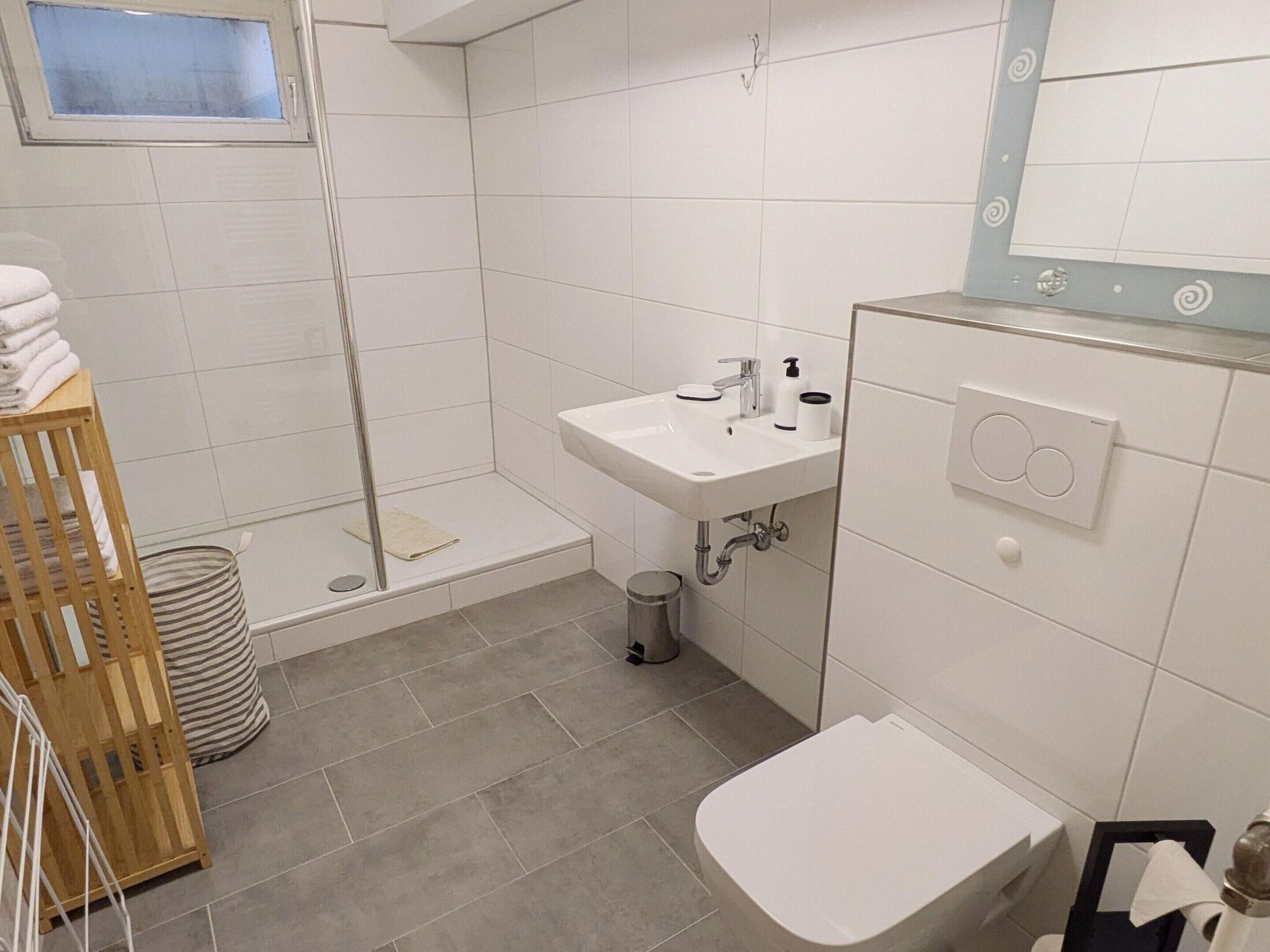 A modern bathroom with a shower, sink, toilet, and a small window.