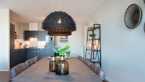 A modern dining area with a long table, cushioned chairs, and a unique woven pendant light. - Apartment in Den Haag for 4 Person (The Hague)