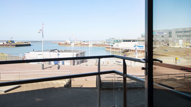 A view from a balcony overlooking a waterfront area with a pier, construction site, and modern buildings. - Apartment in Den Haag for 4 Person (The Hague)