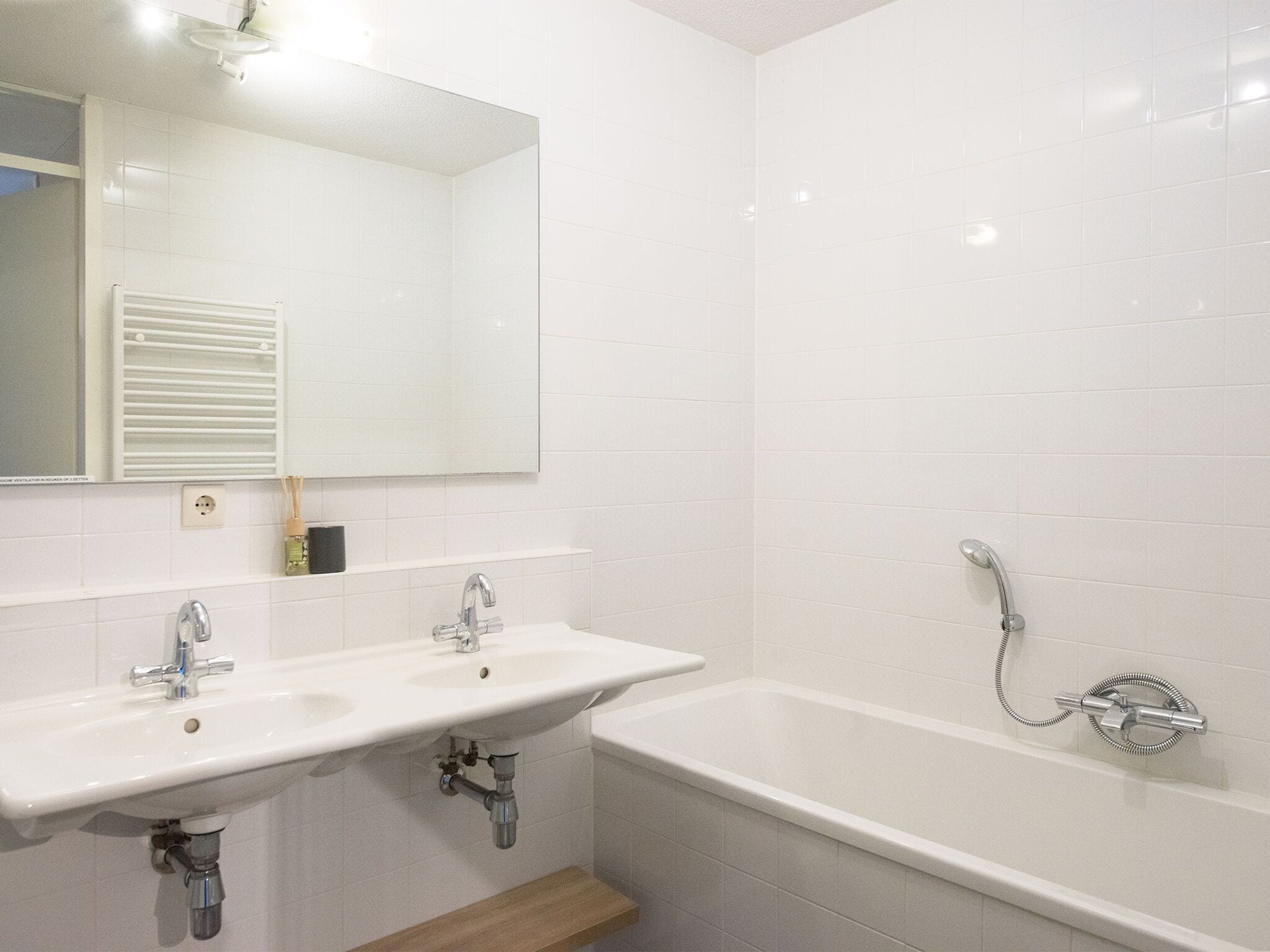 A bathroom with a white sink, a mirror, and a bathtub with a showerhead.