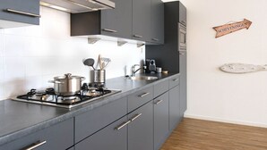 A modern kitchen with grey cabinets, a stainless steel range hood, and a wooden sign on the wall. - Apartment in Netherlands Near the Beach (The Hague)