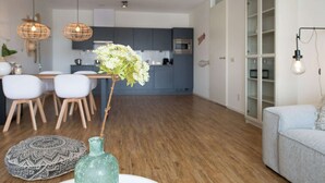 A modern living room with a dining area, kitchen, and built-in shelving. - Apartment in Netherlands Near the Beach (The Hague)