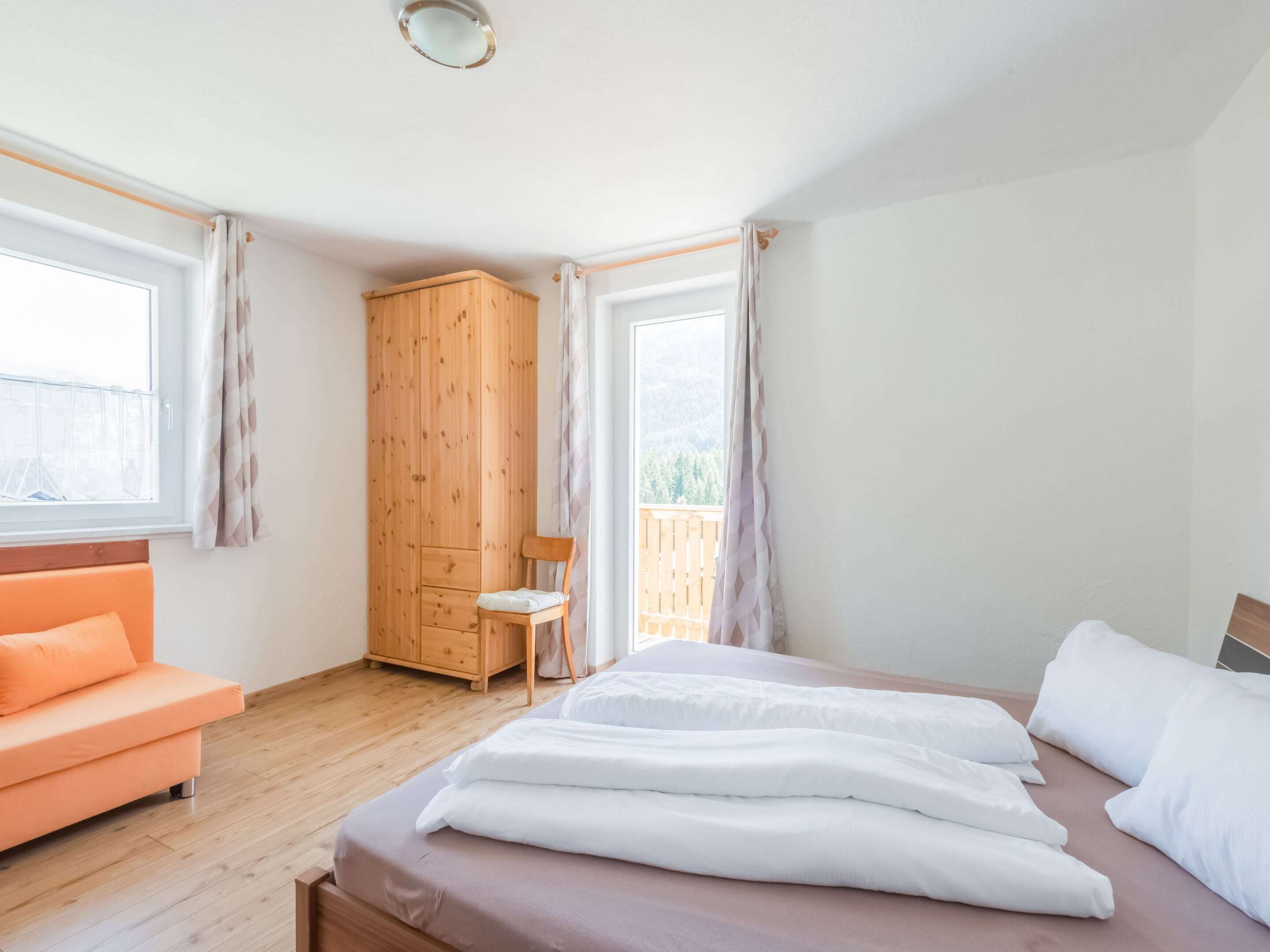 A bedroom with a bed, a wooden wardrobe, a chair, and a sofa.