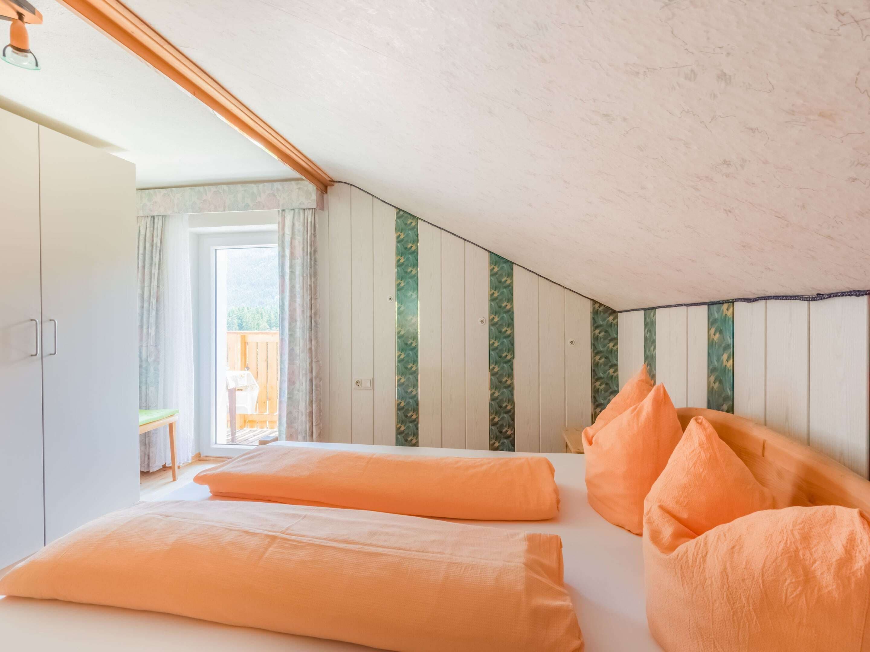 Camera da letto con soffitto spiovente, armadio in legno e vista su un balcone.