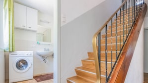 A modern kitchen with a built-in washing machine, a sink, and a staircase with wooden steps and metal railings. - Chalet in Tyrol Near Ski Resort (Fliess)