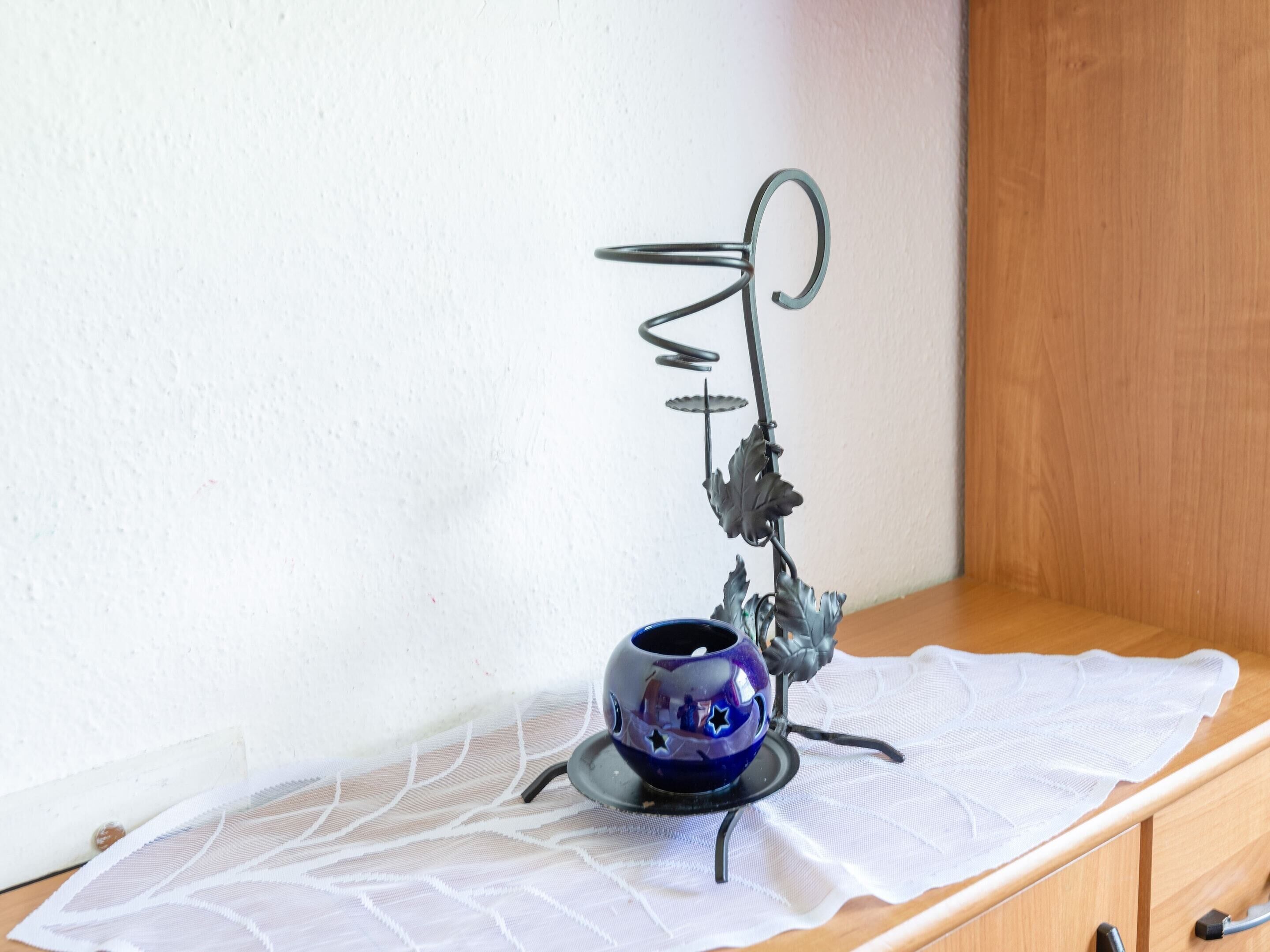 A small table with a decorative metal stand holding a blue ceramic cup, set on a white lace tablecloth.