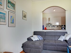 A living room with a grey sofa, a kitchen visible through an archway, and framed pictures on the wall.