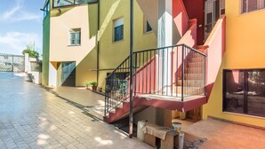 Un edificio de varios pisos con una escalera, plantas en macetas y una entrada protegida por un portón.