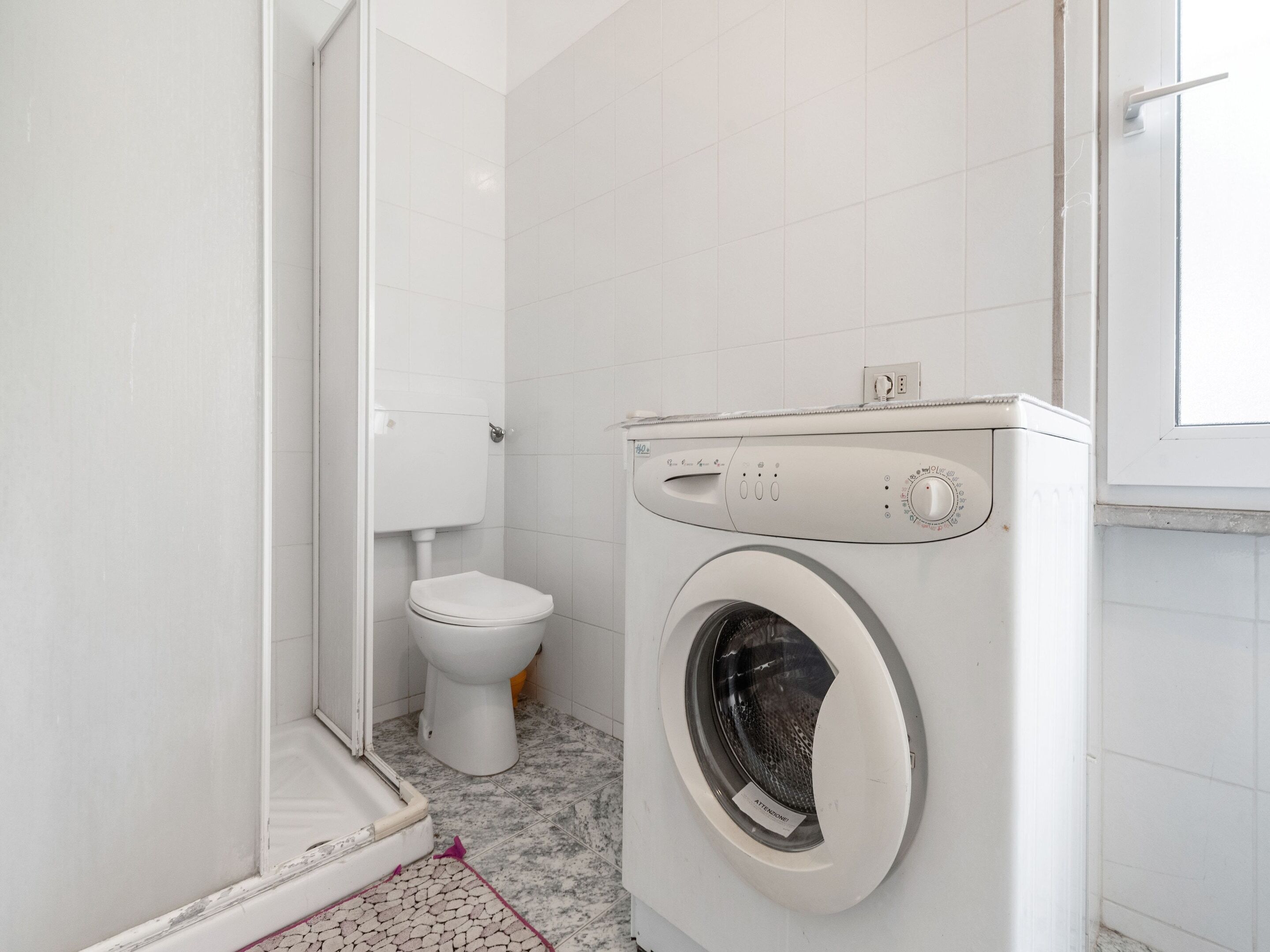 Ein kleines, modernes Badezimmer mit Toilette, Waschmaschine und Duschbereich.