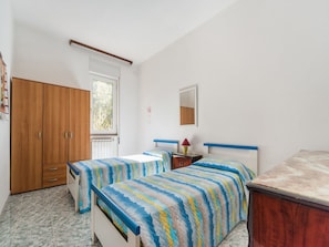 Ein Schlafzimmer mit zwei Einzelbetten, einem Holzschrank, einem Heizkörper und einem Fenster mit Blick auf Bäume.