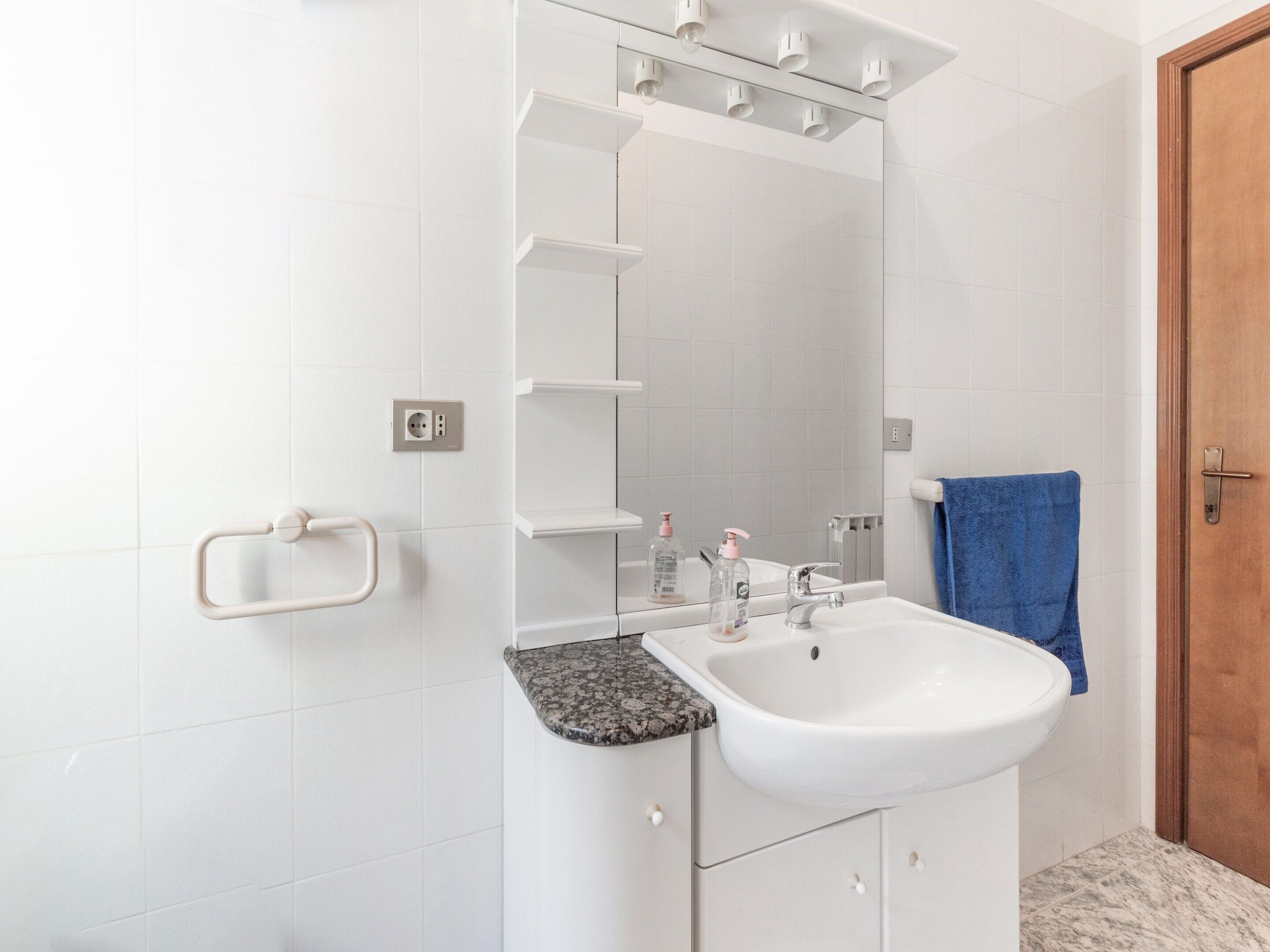 Een badkamer met een witte wastafel, een spiegel en een blauwe handdoek aan de muur.