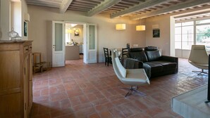 A spacious living area with a high ceiling, exposed wooden beams, a leather sofa, a dining table with chairs, and a kitchen in the background. - Plush Holiday Home in Cortona with Hot Tub (Cortona)