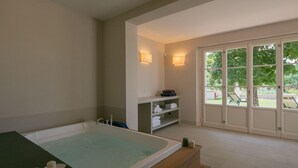 A spa room with a large bathtub, shelves with towels, and a view of the outdoors through a glass door. - Plush Holiday Home in Cortona with Hot Tub (Cortona)