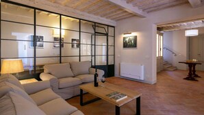 A living room with a sofa, a coffee table, and a wall with framed pictures. There is a staircase leading to another room. - Plush Holiday Home in Cortona with Hot Tub (Cortona)