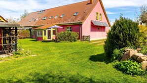 Una casa de color rosa amb teulada vermella i gespa verda.