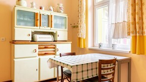 Una cuina amb una estufa antiga, una taula de dinar amb caires i una finestra amb cortines florals.