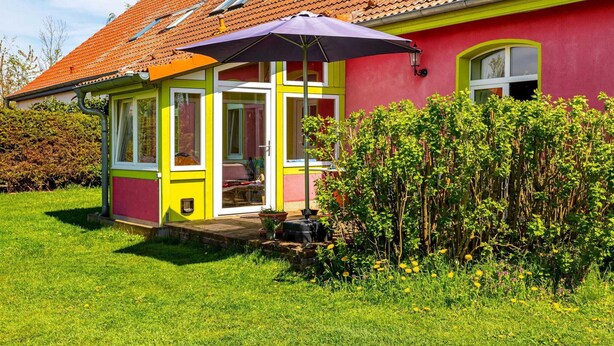 Una casa colorida amb teulades vermelles, un porxo cobert i un jardí ple de flors grogues.
