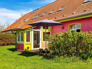 Ein farbenfrohes Haus mit rotem Ziegeldach, einer Veranda und einem Garten mit gelben Blumen.