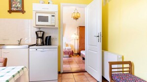 Una cuina compacta amb microones, cafetera i nevera petita. Es veu una taula de dinar amb estovell daurat. Les parets són grogues i el terra, de rajola.