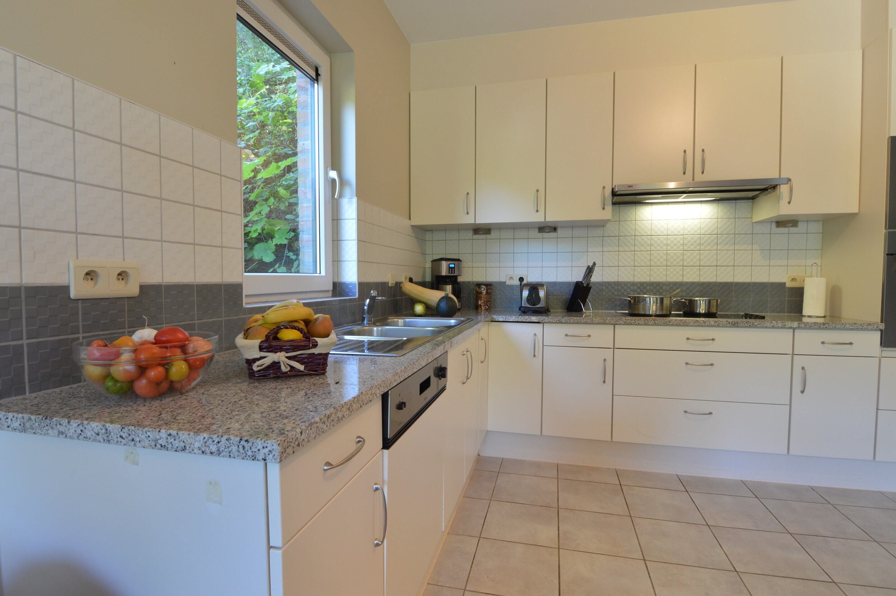 A modern kitchen with white cabinets, a granite countertop, and a window providing natural light.