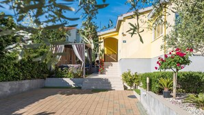 A courtyard with a paved walkway, a covered seating area, and a yellow building with a number sign. - Modern Holiday Home in Zadar With Terrace (Zadar)