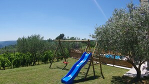 A backyard with a blue slide, a wooden swing set, a pool, and a table with a chair. - Apartment in Croatia Near Adriatic Coast (Barban)
