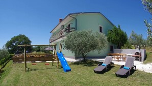 A house with a backyard containing a swing set, a slide, and a barbecue area. - Apartment in Croatia Near Adriatic Coast (Barban)