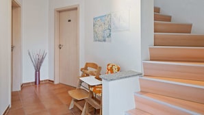 En hall med en trätrappa, en dörr, ett litet bord med en stol och en vas med grenar.