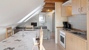 Ett mysigt sovrum på vinden med ett sluttande tak, ett matbord med stolar, en soffa och ett litet kök med spis och diskho.