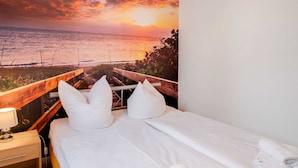 A hotel room with a bed, white bedding, a nightstand with a lamp, and a view of the ocean at sunset. - Restful Holiday Home in Kalkhorst near Beach & City Center (Kalkhorst)