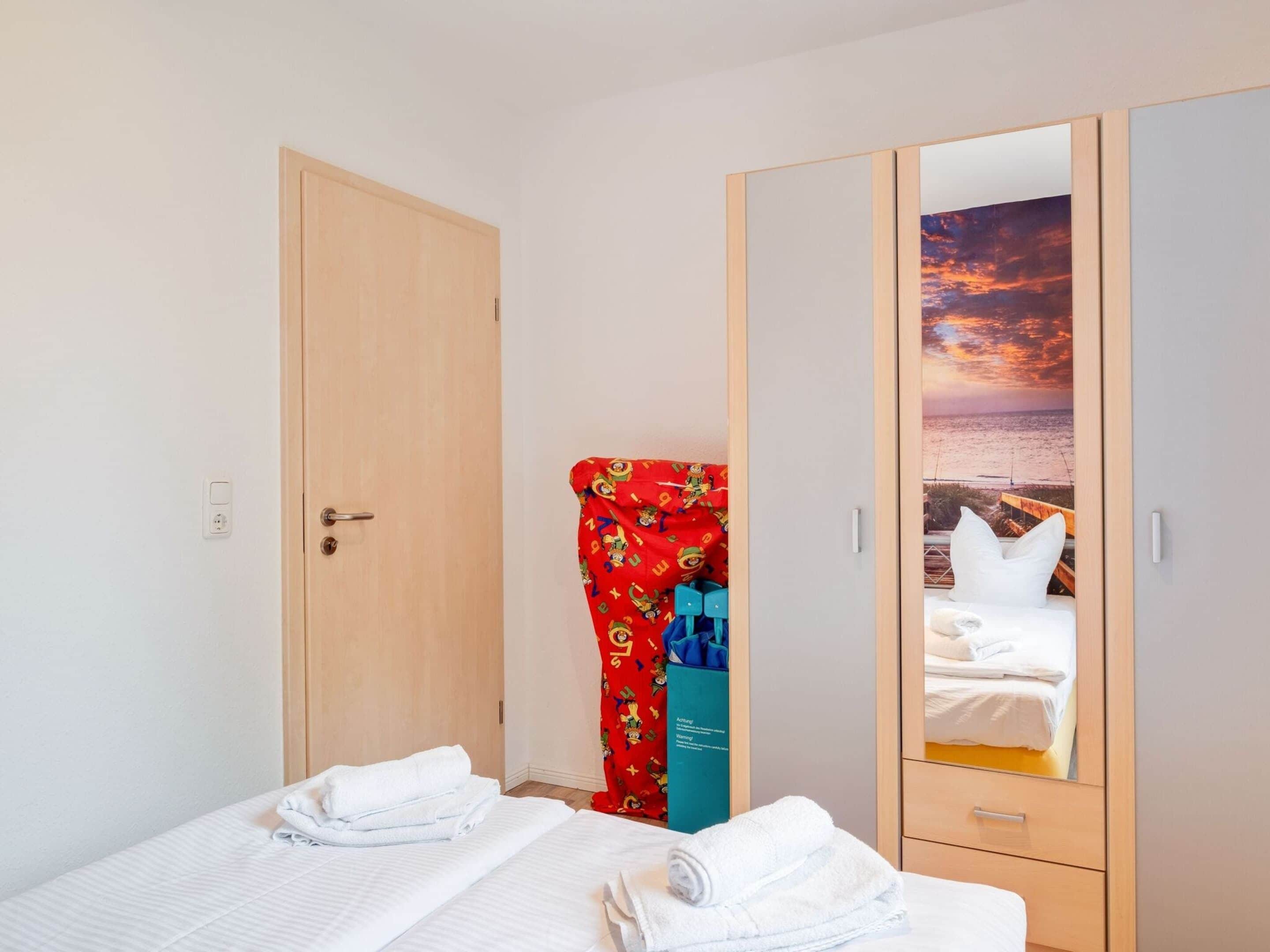 A hotel room with a bed, a wardrobe, and a mirror reflecting a sunset view.