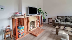 A living room with a brick fireplace, a television on a stand, a sofa, a coffee table, and a small wooden side table. - The Waltz of the Chickadees in Somme Leuze (Somme-Leuze)