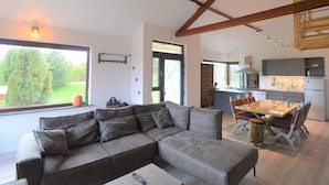 A modern living room with a sectional sofa, a dining table with chairs, and a kitchen in the background. - The Waltz of the Chickadees in Somme Leuze (Somme-Leuze)