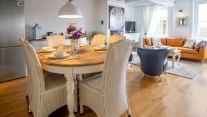A dining area with a round wooden table, white wicker chairs, and a vase with purple flowers. - Holiday Home in Stavele With Terrace (Alveringem)