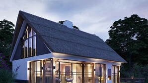 A modern house with a thatched roof, large glass windows, and a well-lit interior. - Luxury Villa With Sauna Near the Beach (De Cocksdorp)