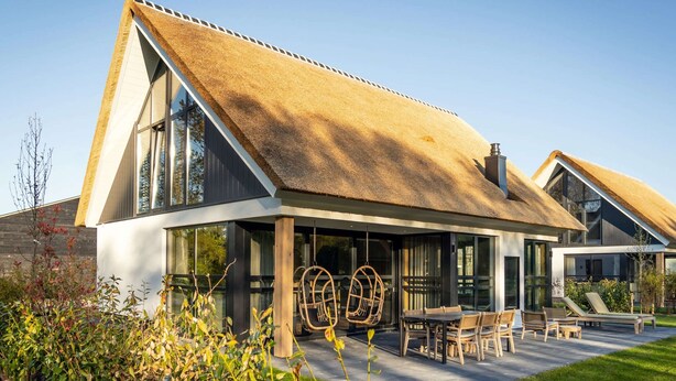 A modern house with a thatched roof, large windows, and a patio with outdoor furniture. - Luxury Villa With Sauna Near the Beach (De Cocksdorp)