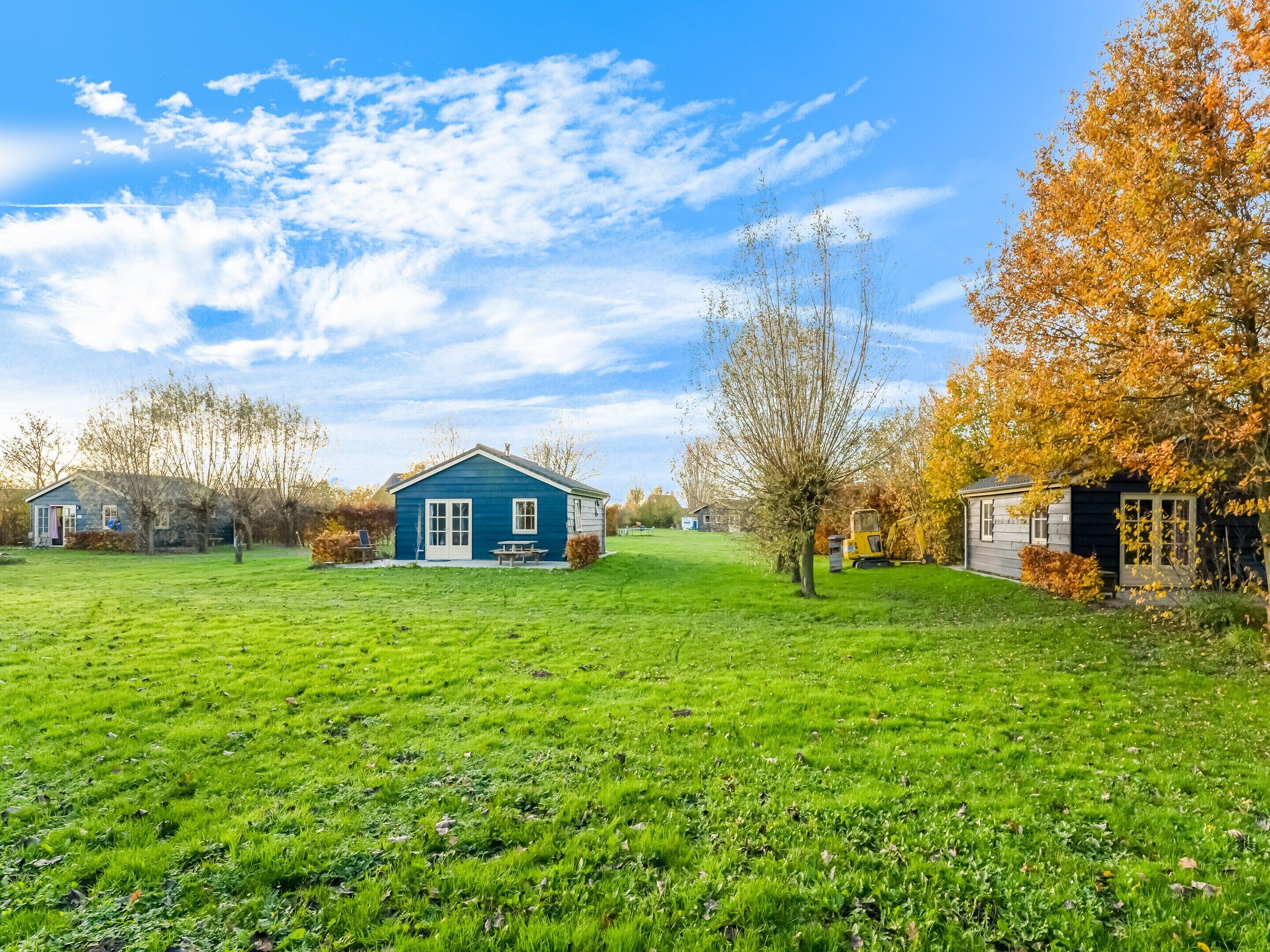 Een blauw huis met een witte deur en ramen, omringd door een groen gazon en bomen met herfstbladeren.