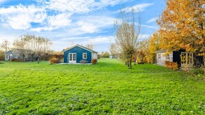 A blue house with a white door and windows, surrounded by a green lawn and trees with autumn leaves.