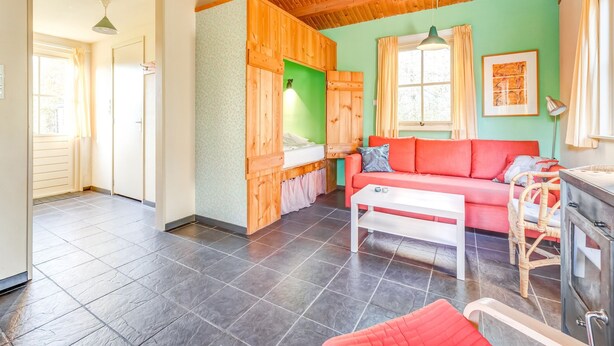 A cozy room with a wooden ceiling, a red sofa, a white table, and a green wall.
