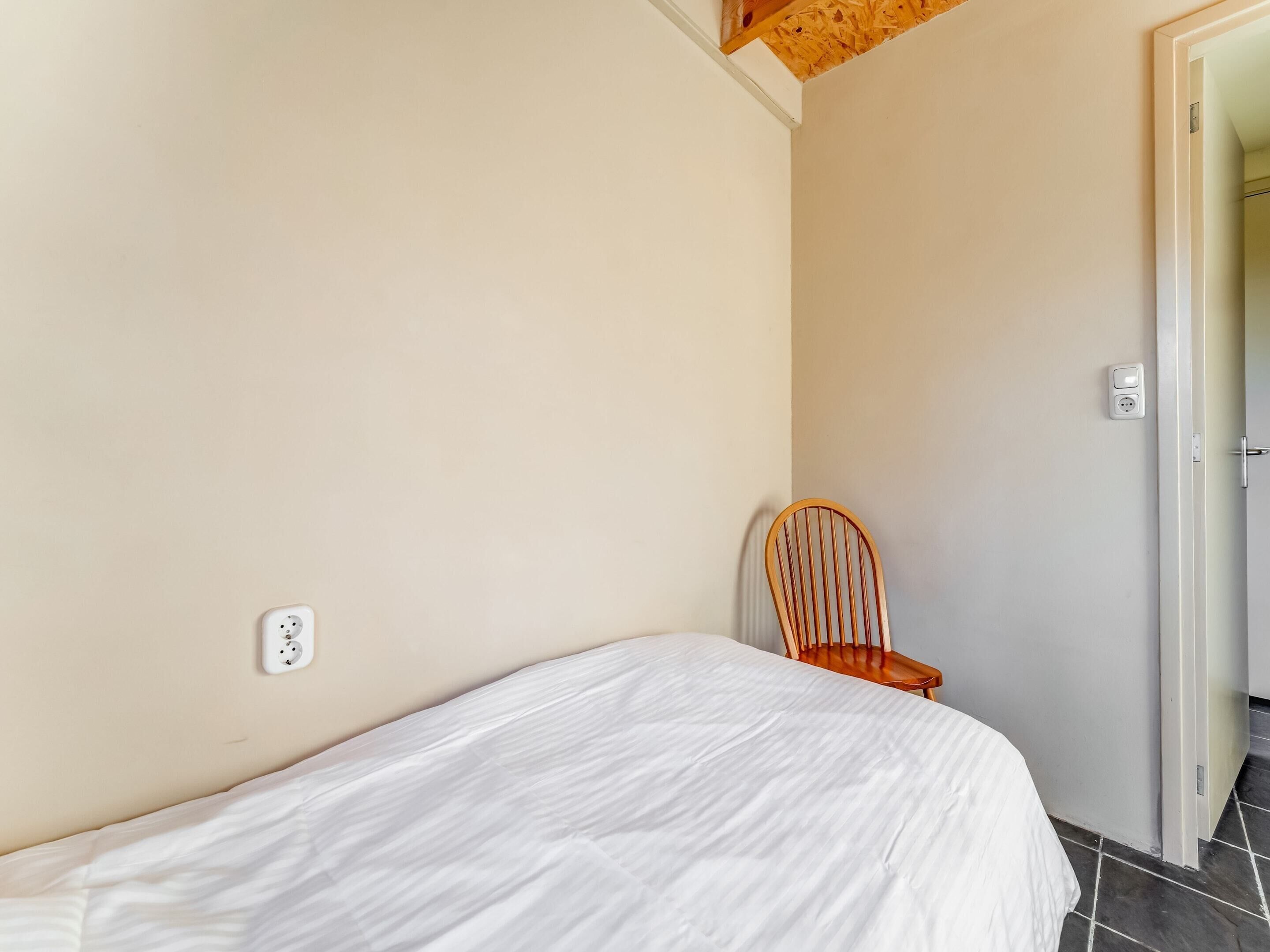 A bedroom with a single bed, a wooden chair, and a door leading to another room.