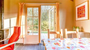 A room with a wooden table, a red chair, a bench, and a view of the outdoors through a glass door.